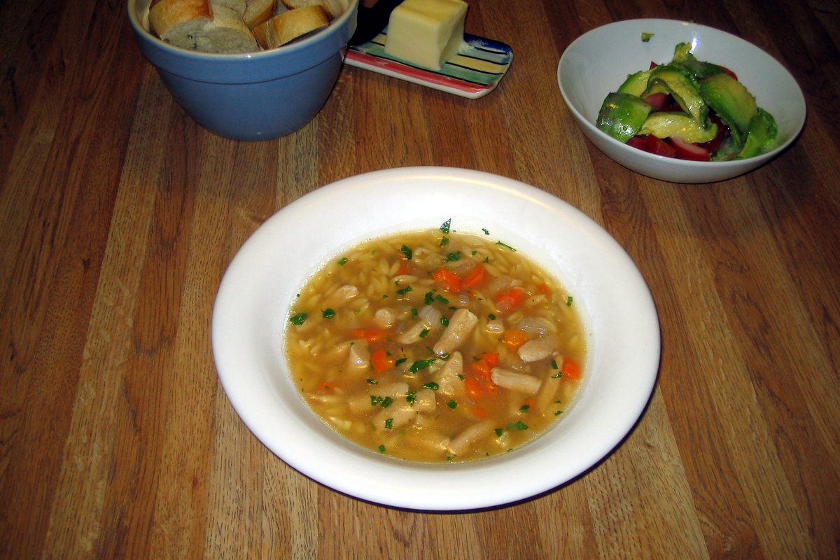 Bowl of lemon chicken orzo soup on a wooden table