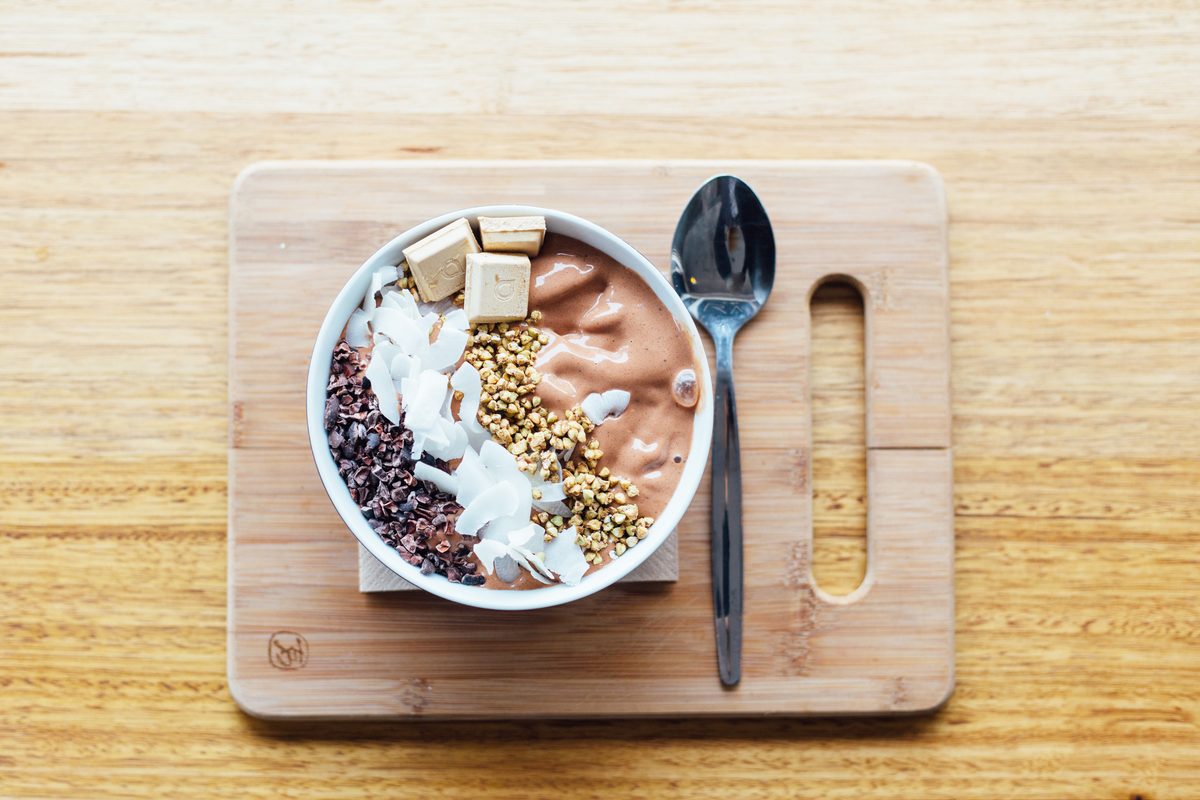 Smoothie bowl topped with granola and coconut on a wooden board